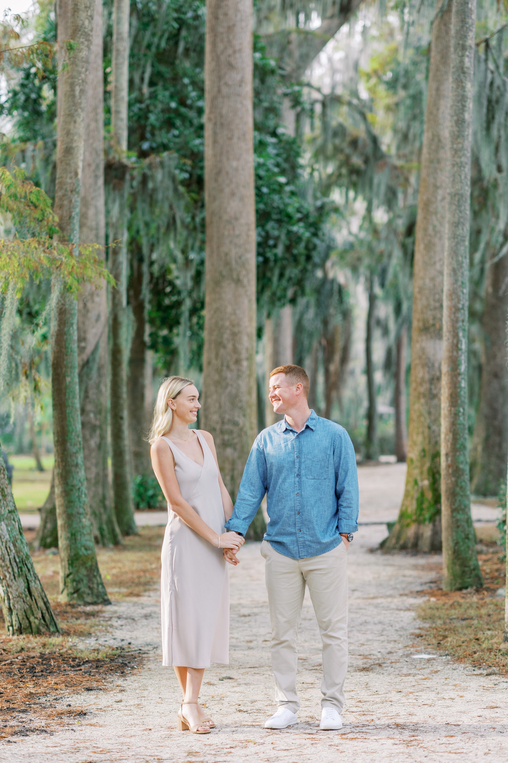 couple smiles at one another among tall trees in this Winter Park Engagement Session