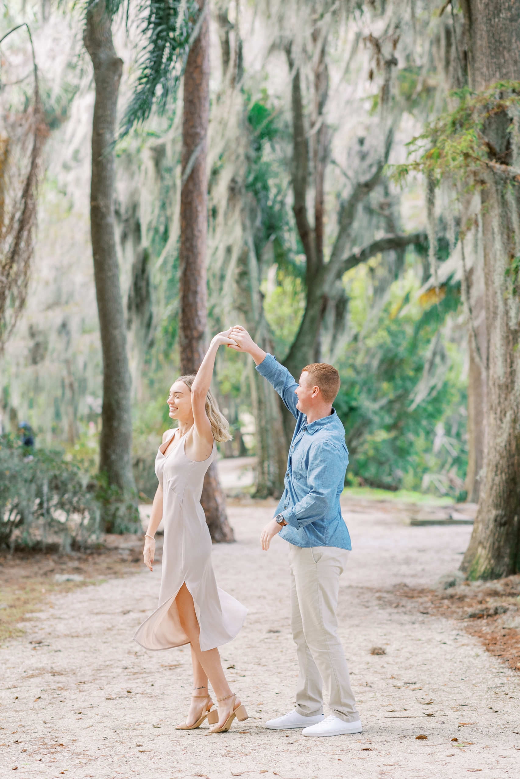 couple twirls on white gravel path with streaming sunlight in this Winter Park Engagement Session