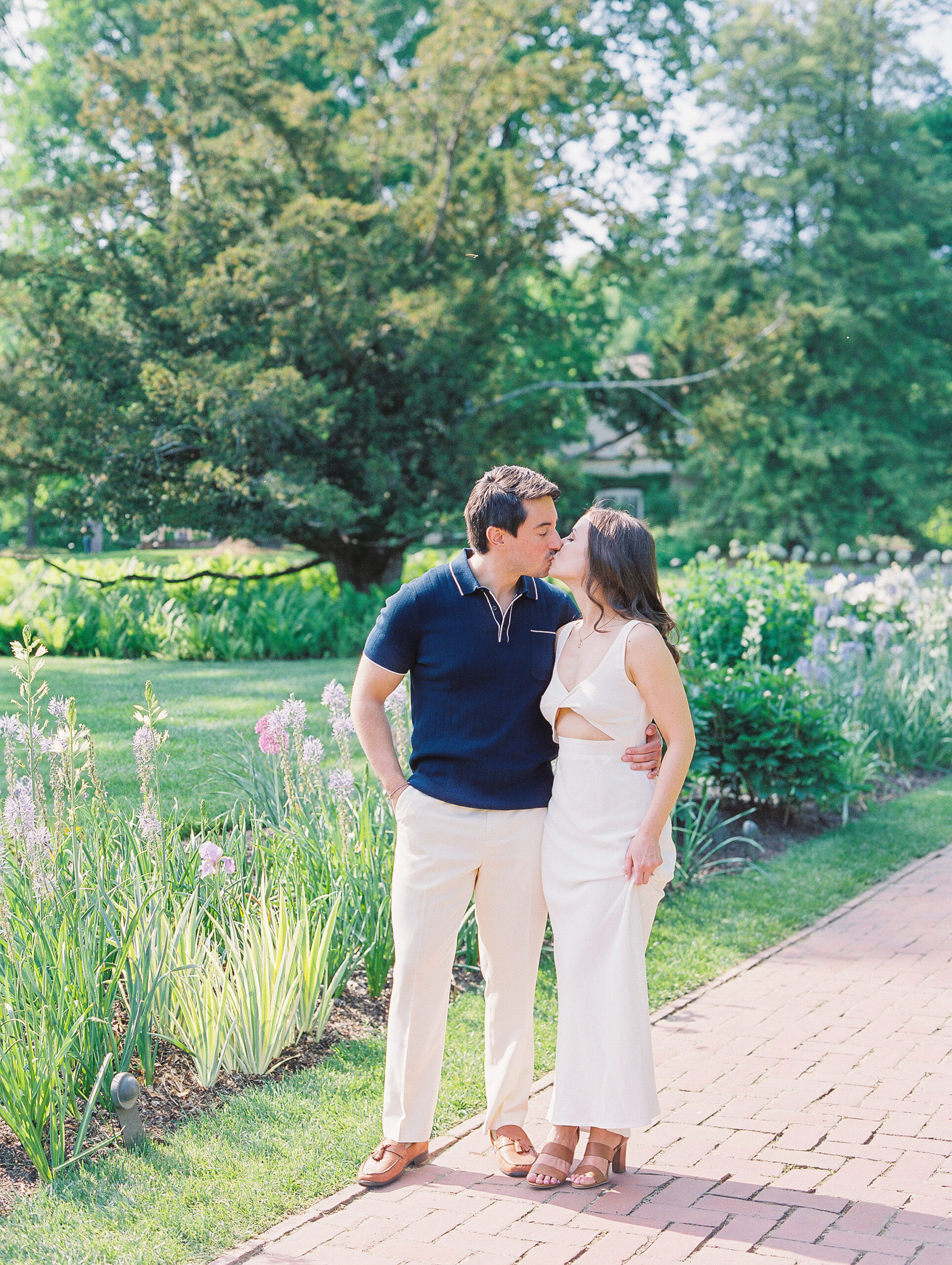 Spring Longwood Gardens Engagement Session shot on film by destination wedding photographer Katie Trauffer - couple kisses in front of manicured garden