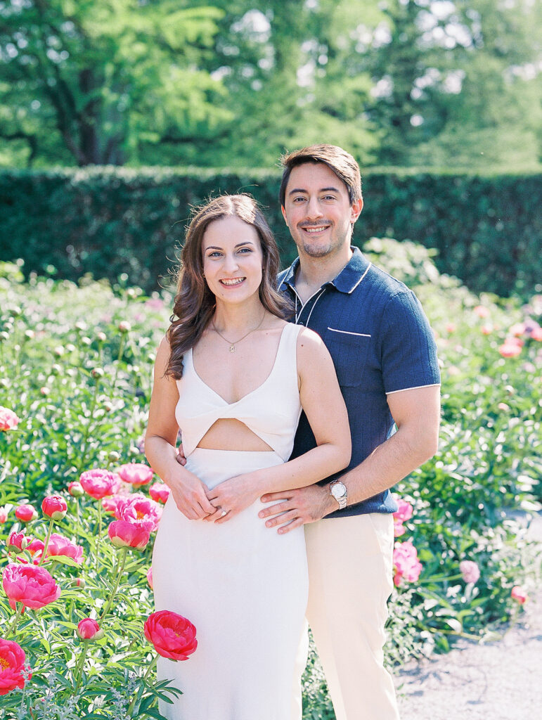 couple stands together in peony garden with green trees