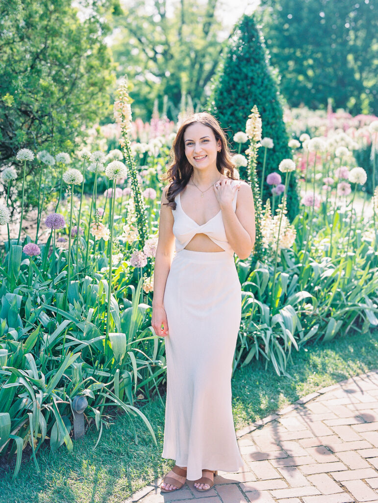 Spring Longwood Gardens Engagement Session shot on film by destination wedding photographer Katie Trauffer - woman stands in front of flowers wearing cream dress