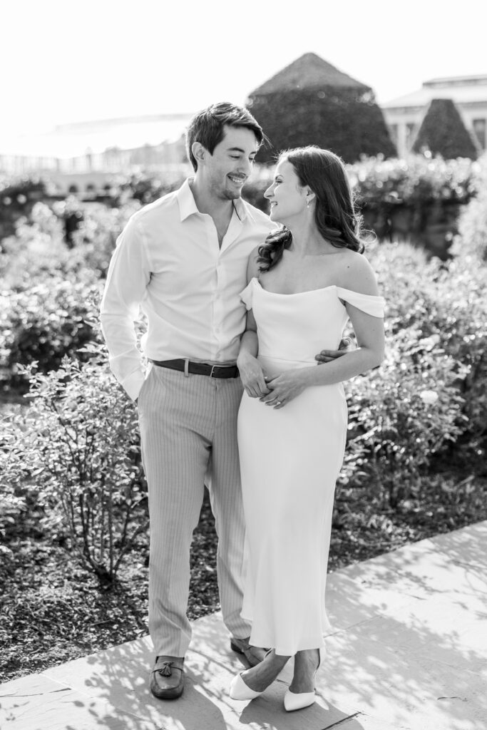 couple stands in front of rose bushes in black and white