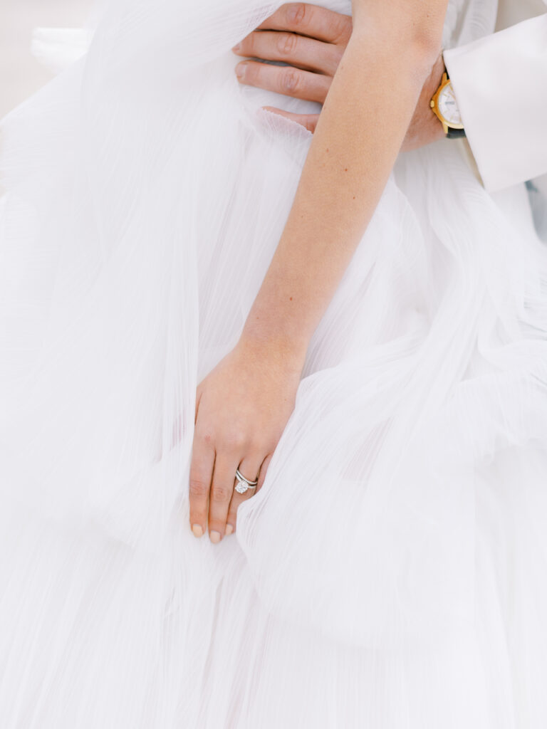 bride and groom hands amid ruffled layers of wedding dress