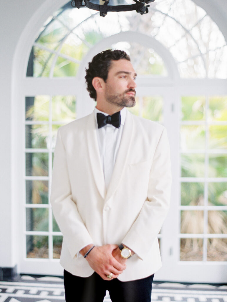 groom portrait at luxury charleston wedding standing in front of large window with palm trees behind