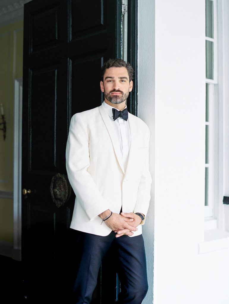groom portrait leaning against historic doorway at luxury charleston wedding