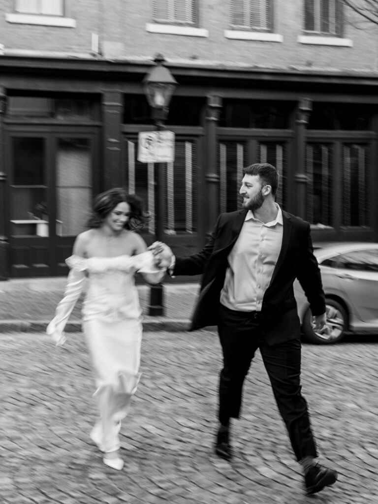 engaged couple energetically walks across cobblestone downtown street