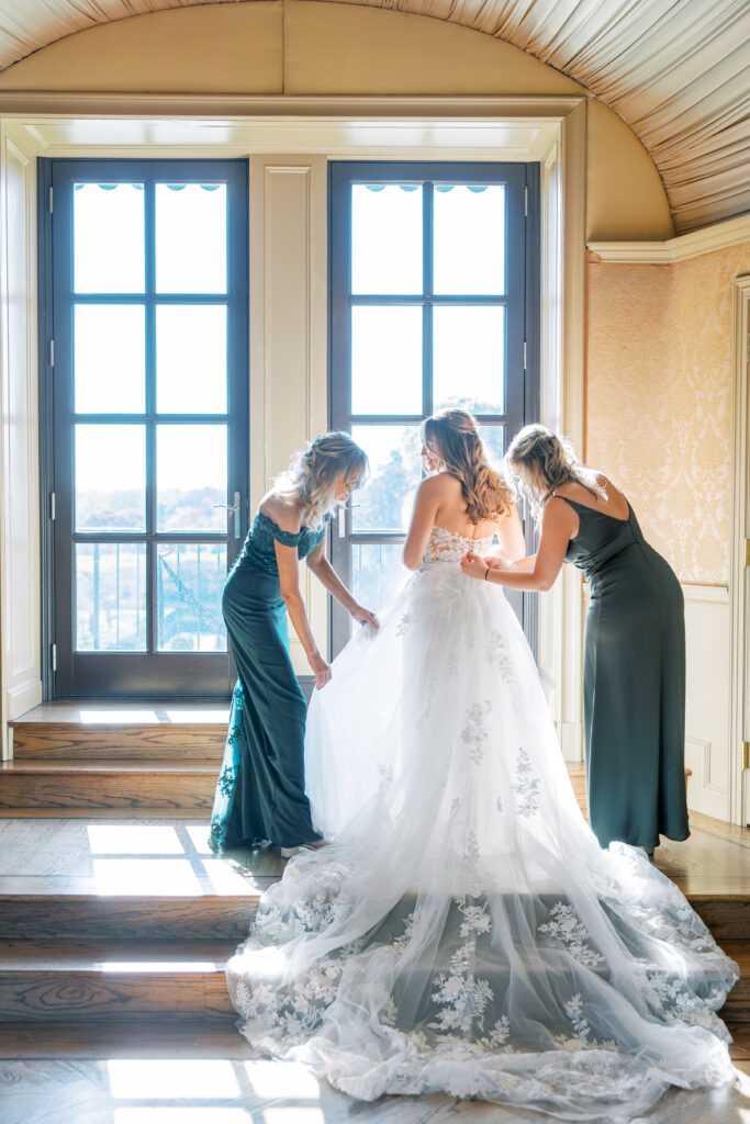 bride getting in wedding dress with mother and sister in green dresses