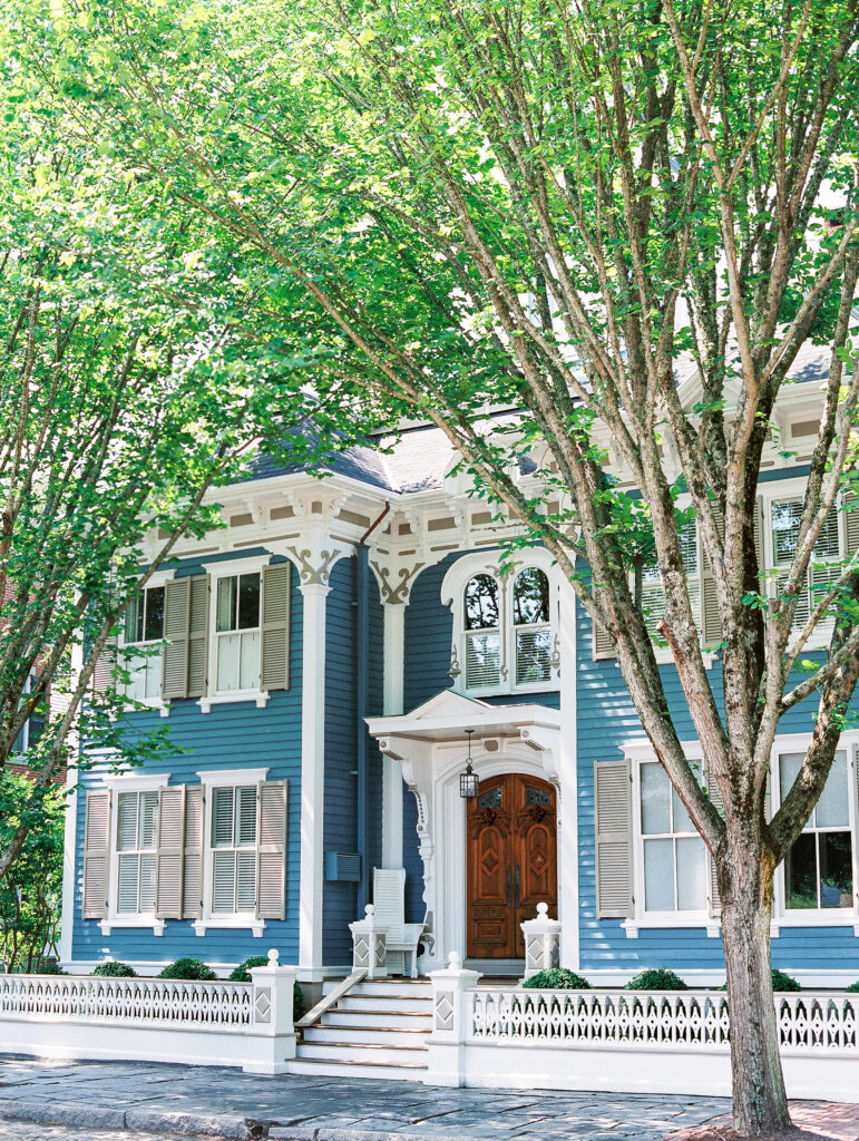 historic blue house on sun dappled street with green trees