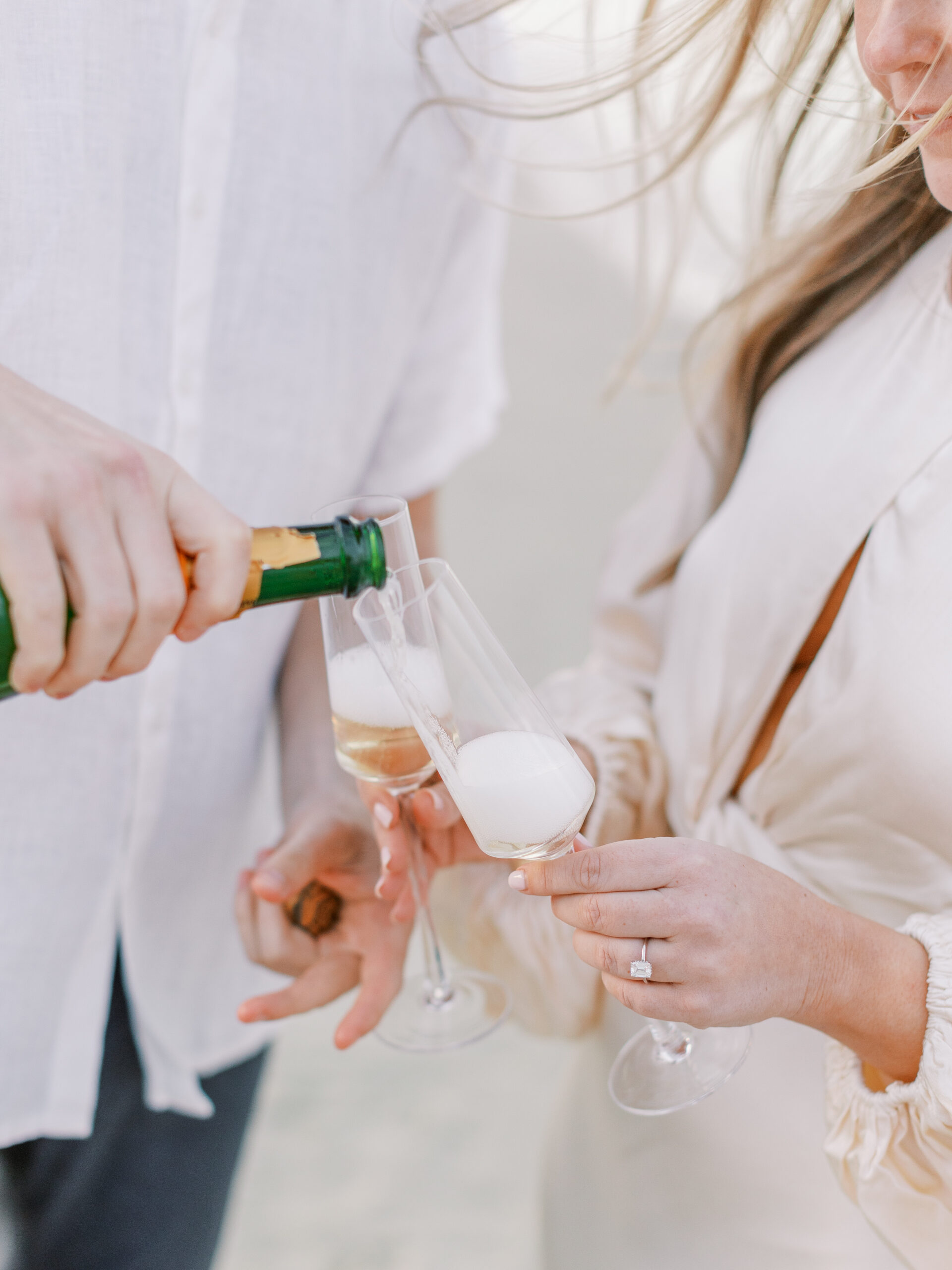 Lewes Beach Engagement Session Couple pours champagne on breezy beach