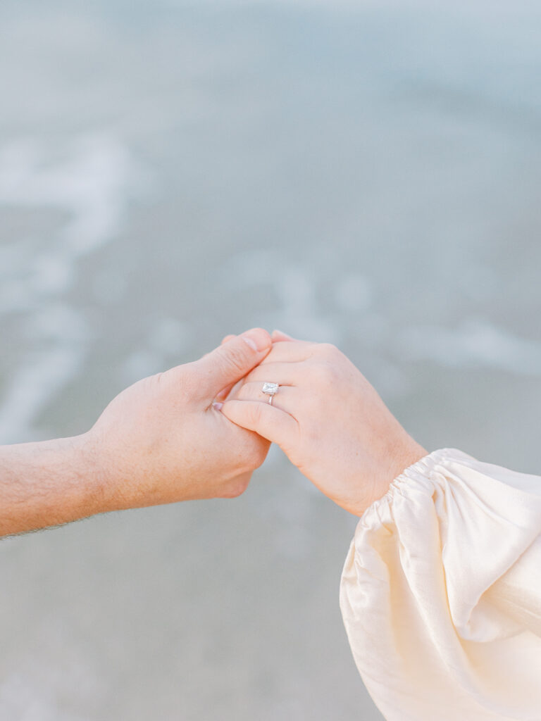close up of engaged couple holding hands on beach