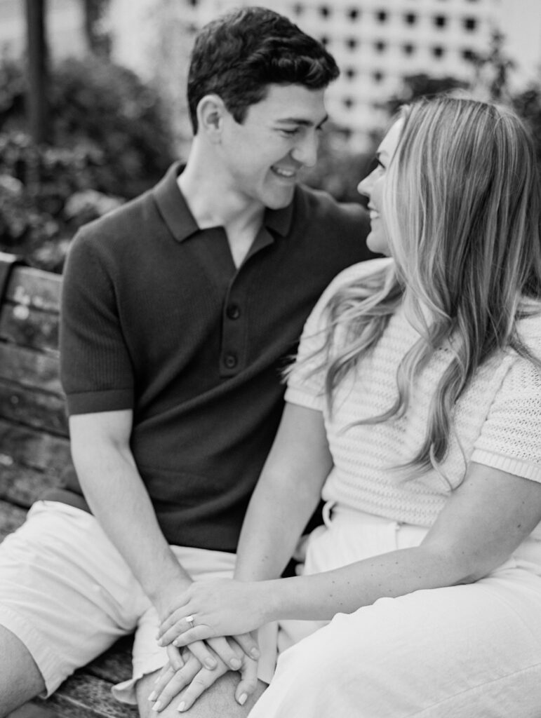 couple smiles at each other sitting on bench in black and white