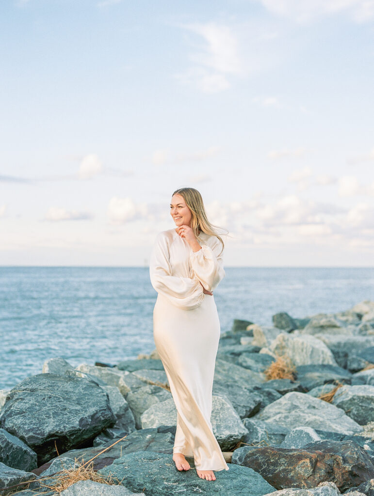 bride stands on rocky outcrop in front of blue ocean