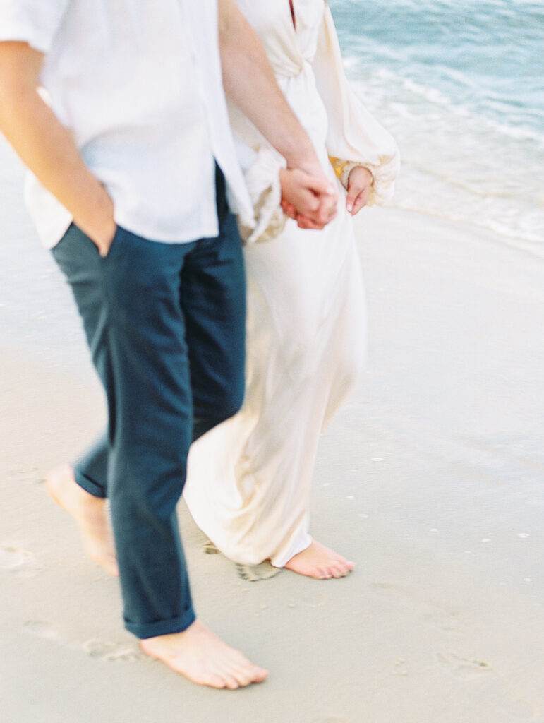 Lewes Beach Engagement Session Couple walks hand in hand along water's edge