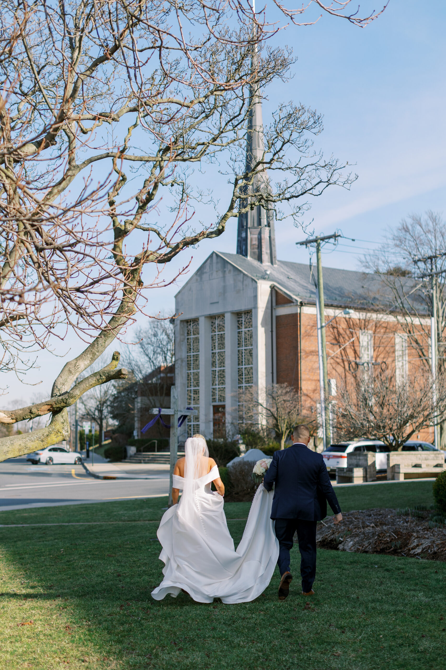 bride and groom walk across church lawn on wedding day