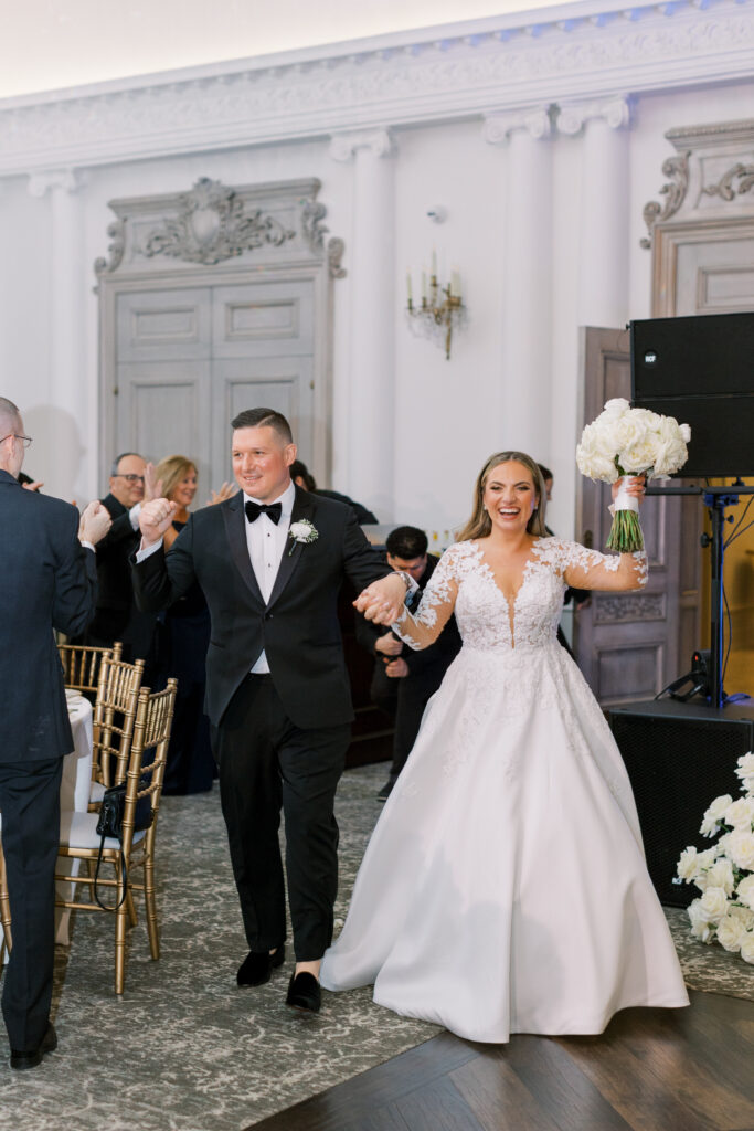 bride and groom joyfully enter wedding reception in large white ballroom