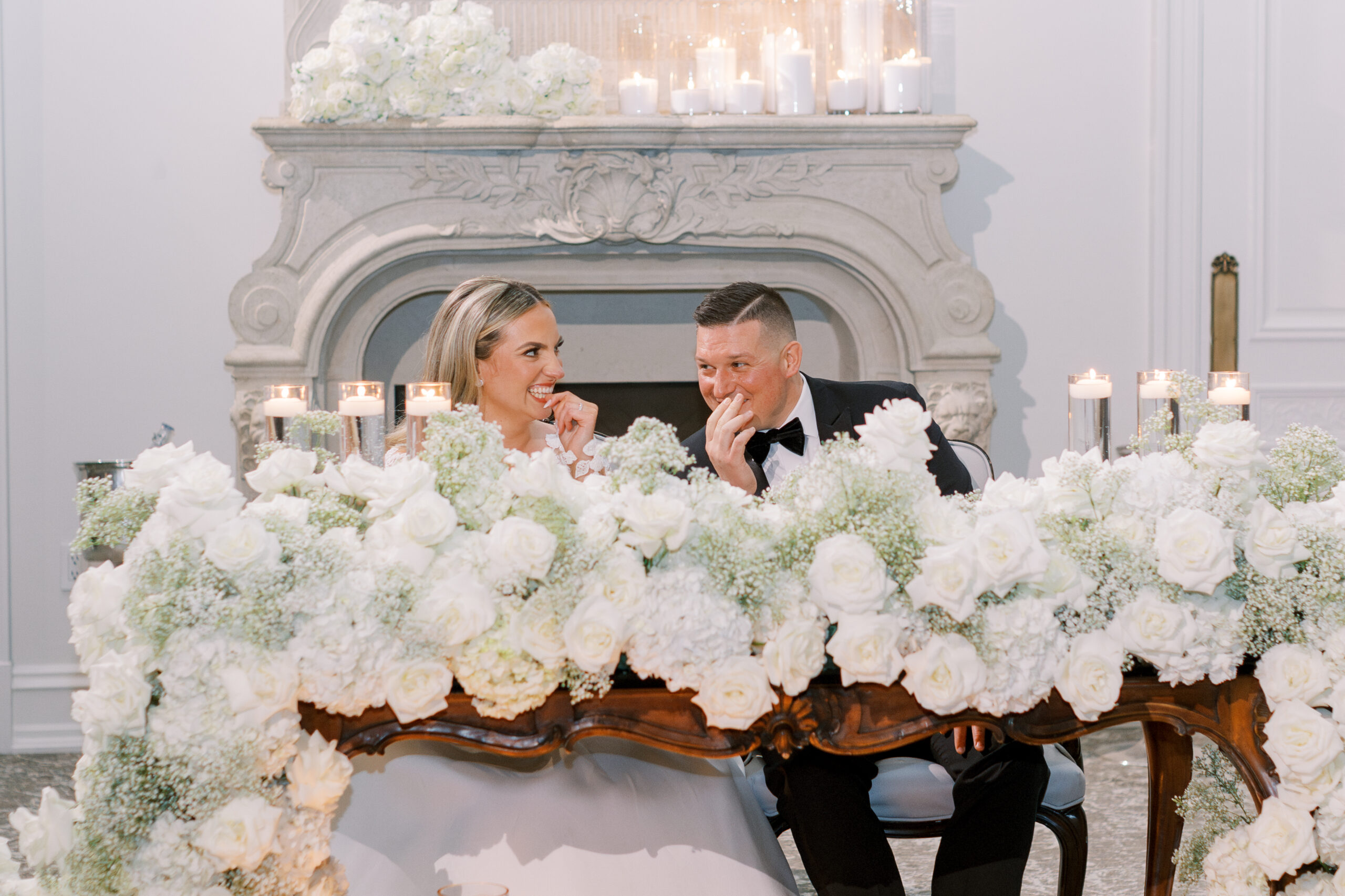 bride and groom laugh at one another sitting at flower covered table