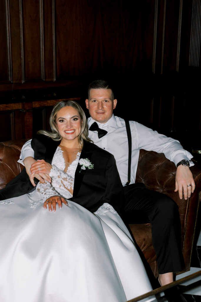 bride and groom lounge on leather couch during reception
