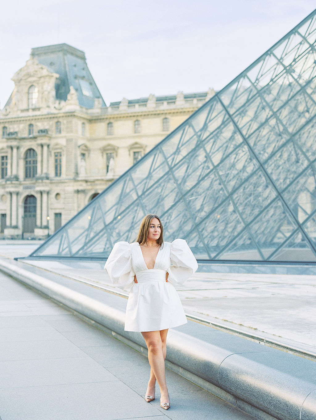 Bride in white dress standing in front of Louvre pyramid at Paris Engagement Photoshoot