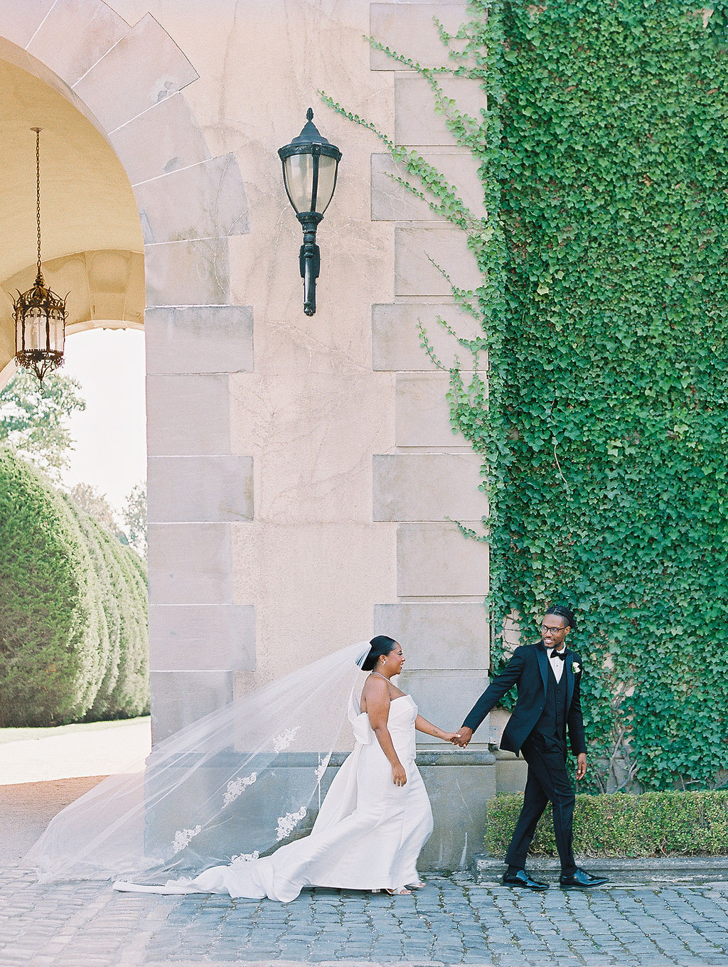 bride and groom walk by ivy covered wall Oheka Castle Wedding Photography