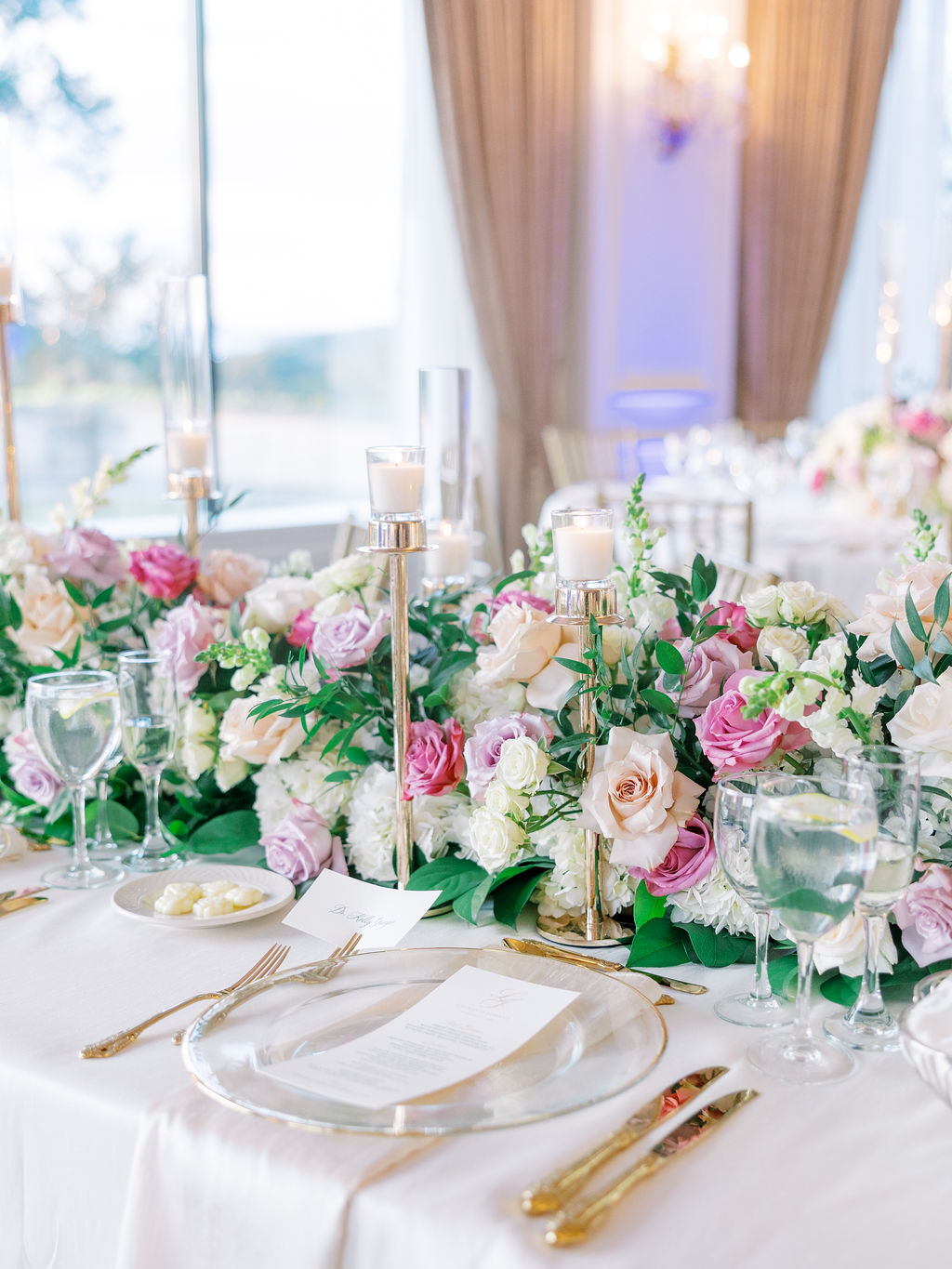 Oheka Castle Wedding Photography reception table covered in blush and mauve roses with candles and gold flatware